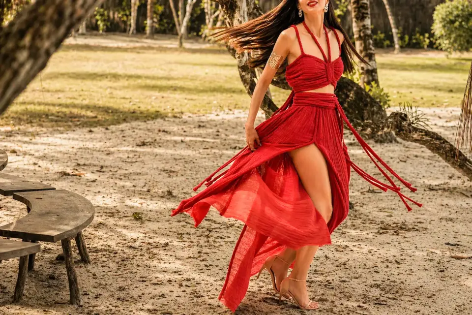Elegant luxury escort in a flowing red dress in a warm outdoor setting, enhancing a refined experience for couples
